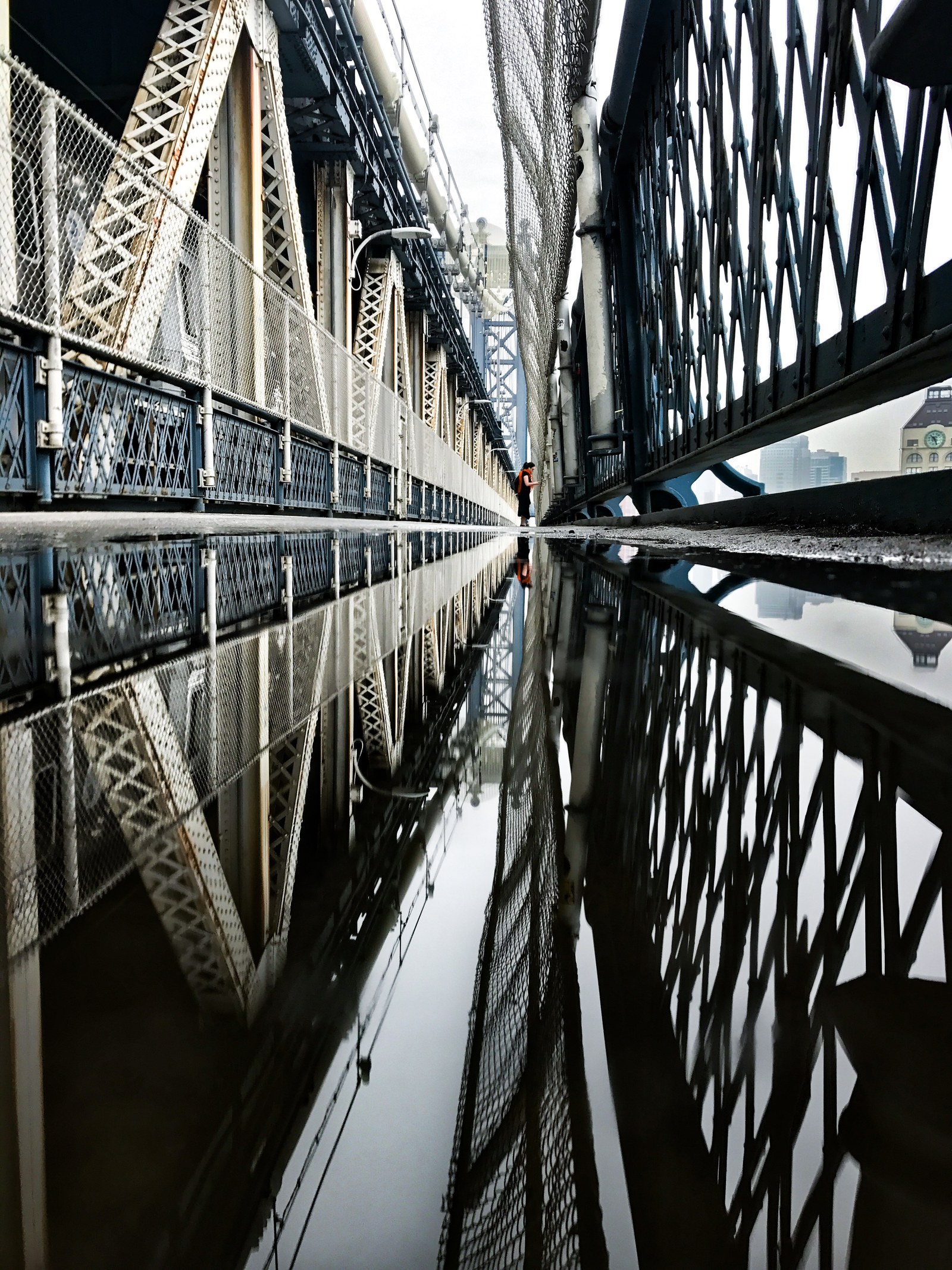 A New York bridge caught upside down in a puddle, a small figure walking in the distance.