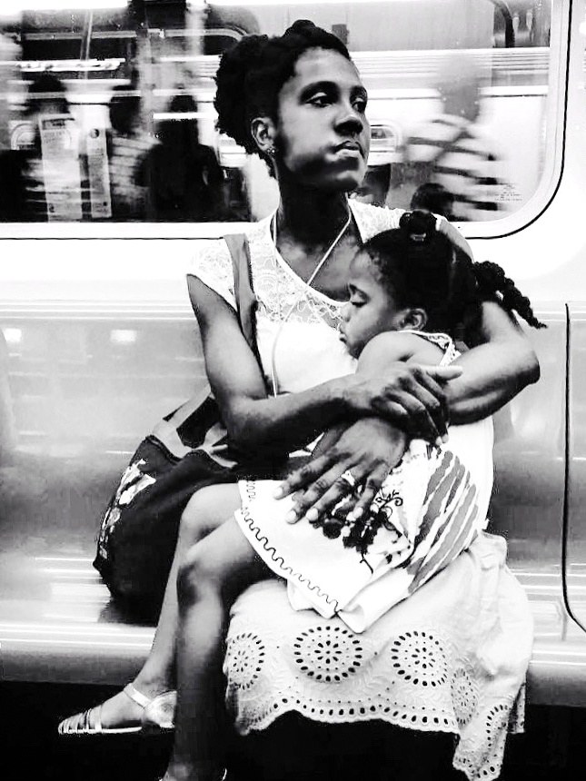 A mother holding her sleeping child on the subway.