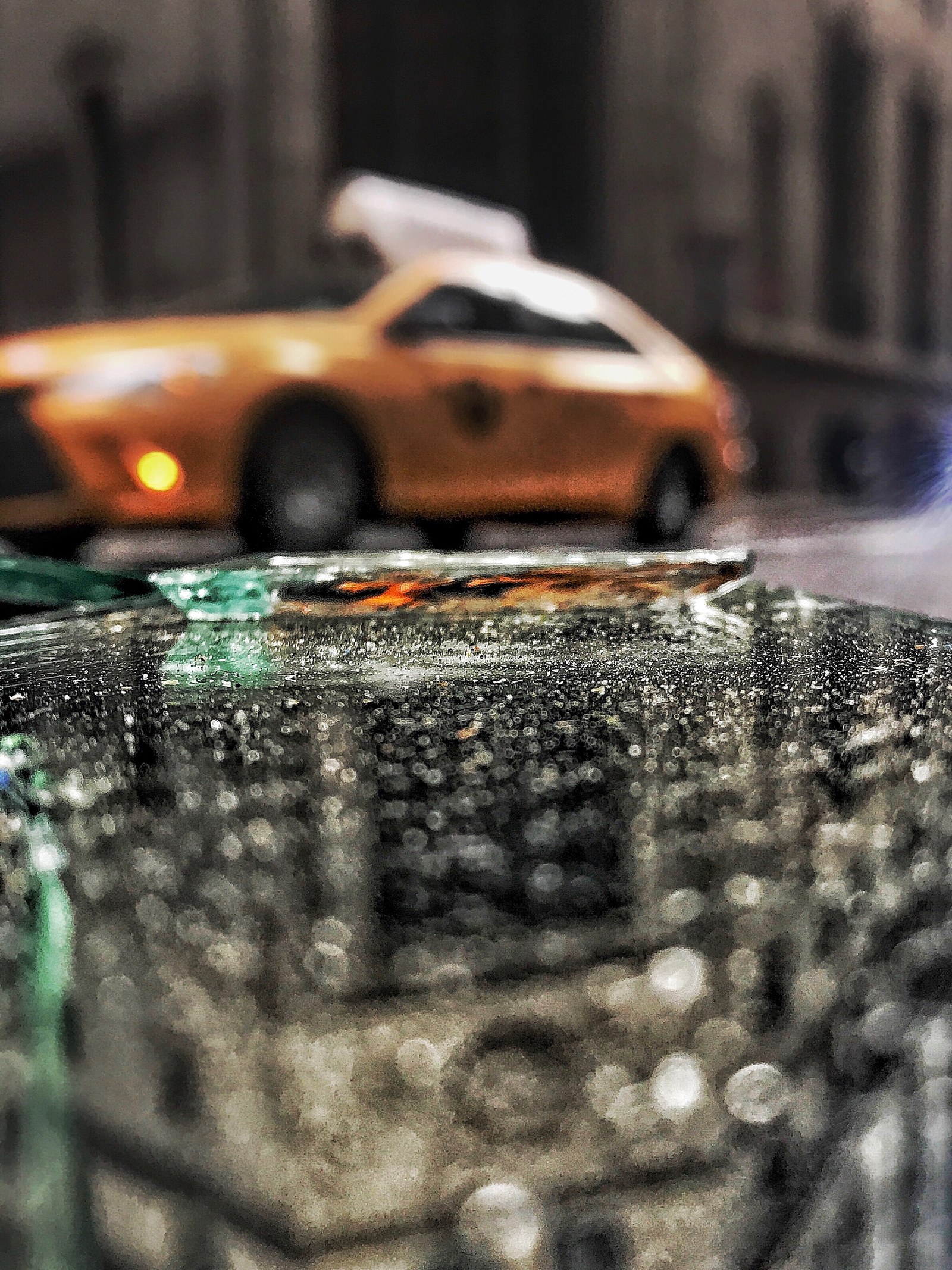A yellow New York taxi blurred beyond wet, broken glass in the foreground.