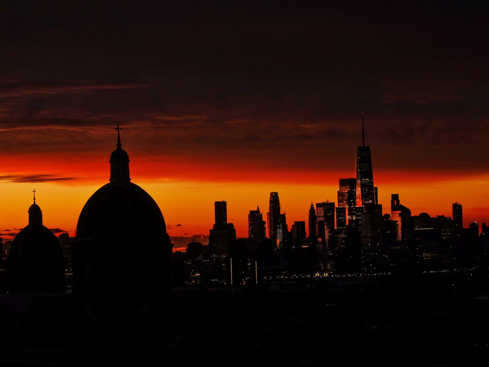 Two church domes in silhouette against an orange horizon, with the towers of the city lit beyond them.