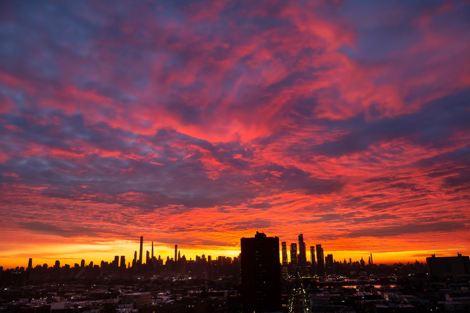 A vast sky of red and violet cloud over the whole skyline at sunrise, a single dark tower standing in the foreground.