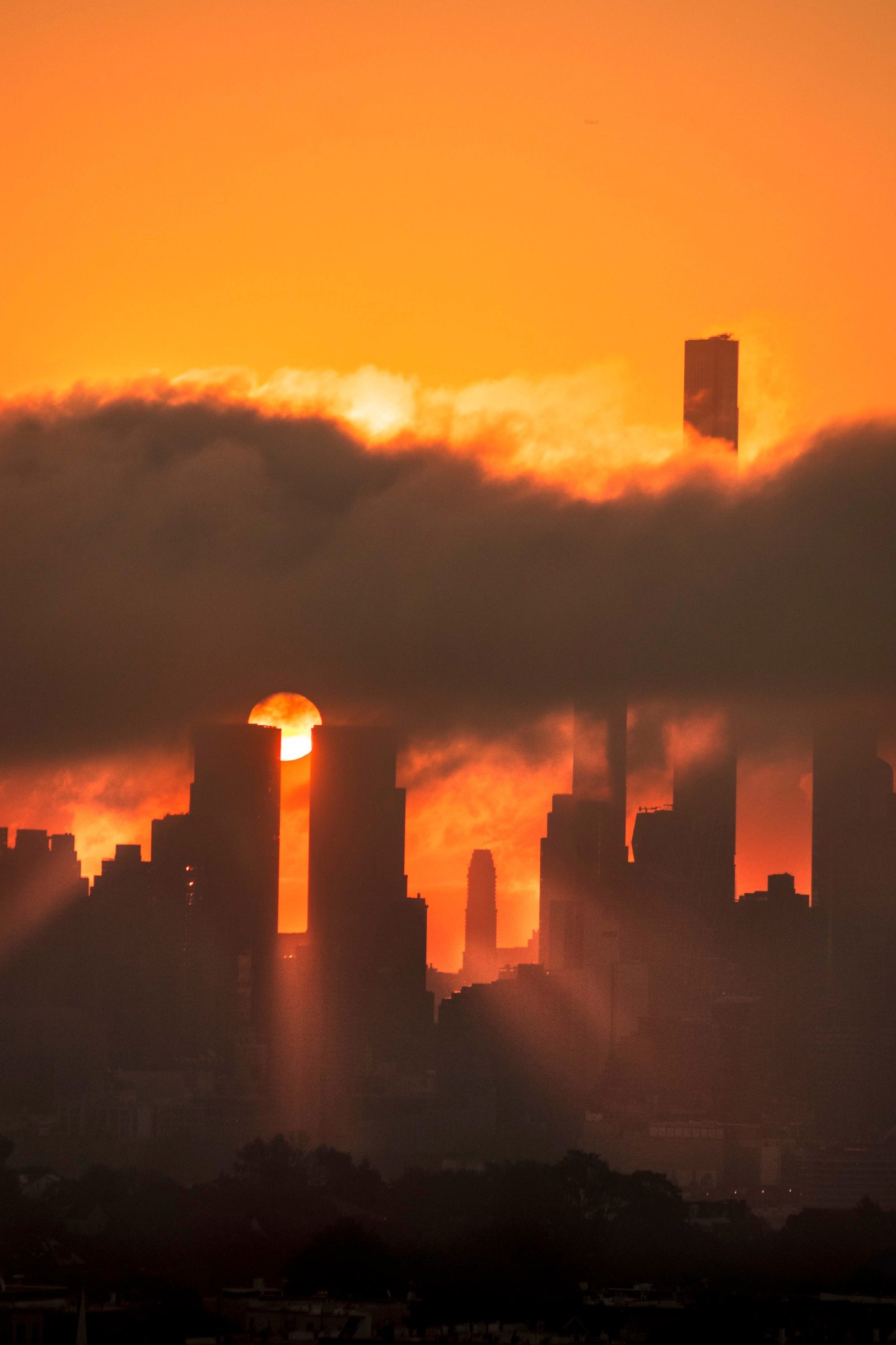 The sun caught between two towers beneath a heavy band of cloud, the city dissolving into orange haze.